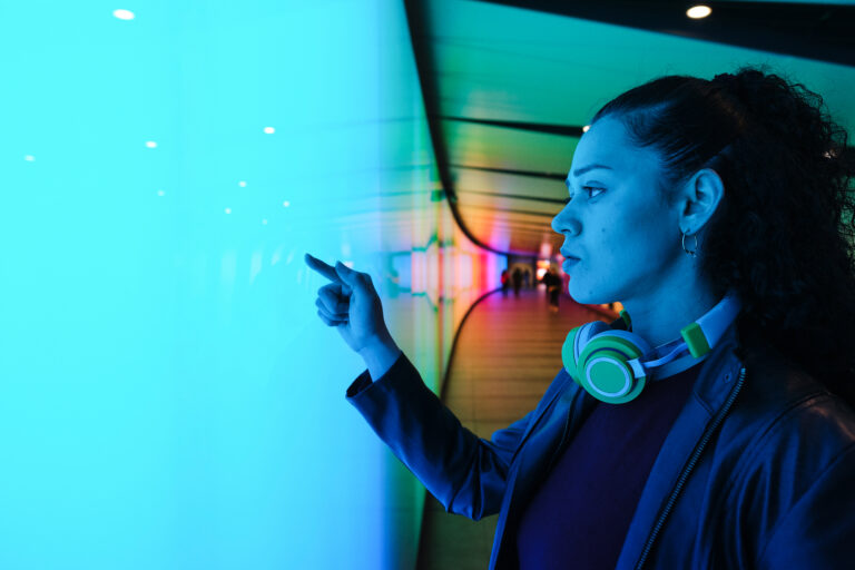 Young woman wearing headphones is touching a large interactive touchscreen in a futuristic tunnel